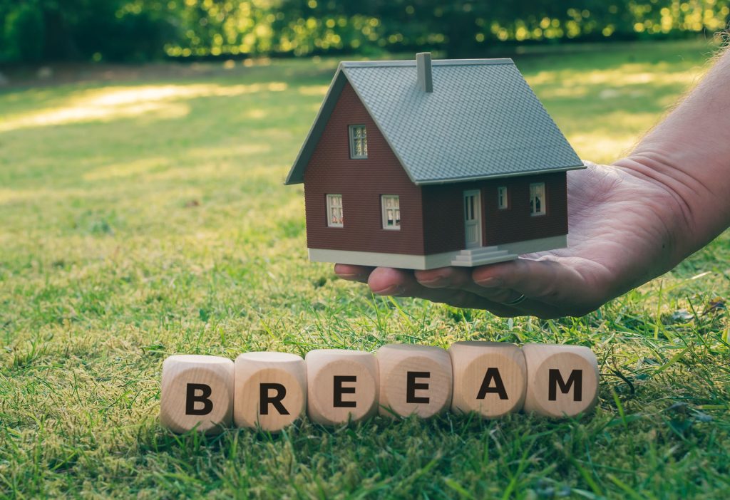 BREEAM Certification and Pre-Demolition Audits: What You Need to Know this image shows the word BREEAM in wooden blocks sitting on grass, a hand is extended above holding a model house